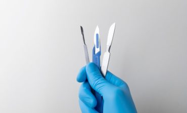 hand-with-rubber-glove-holding-medical-scalpel_23-2149299266